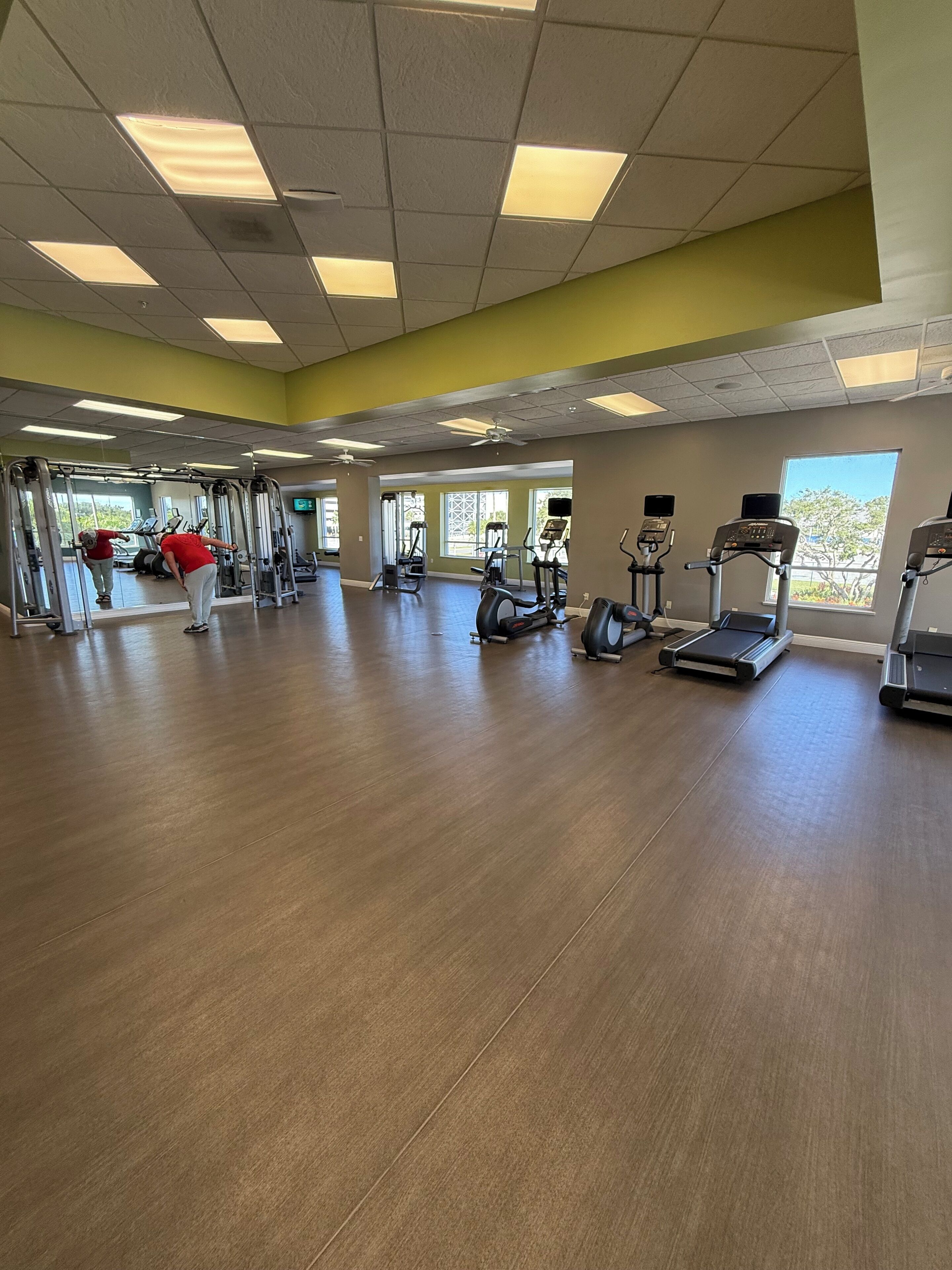 Ein geräumiges Fitnessstudio mit verschiedenen Trainingsgeräten, großen Fenstern und einem Holzboden.