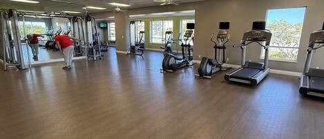 Ein geräumiges Fitnessstudio mit verschiedenen Trainingsgeräten, großen Fenstern und einem Holzboden.