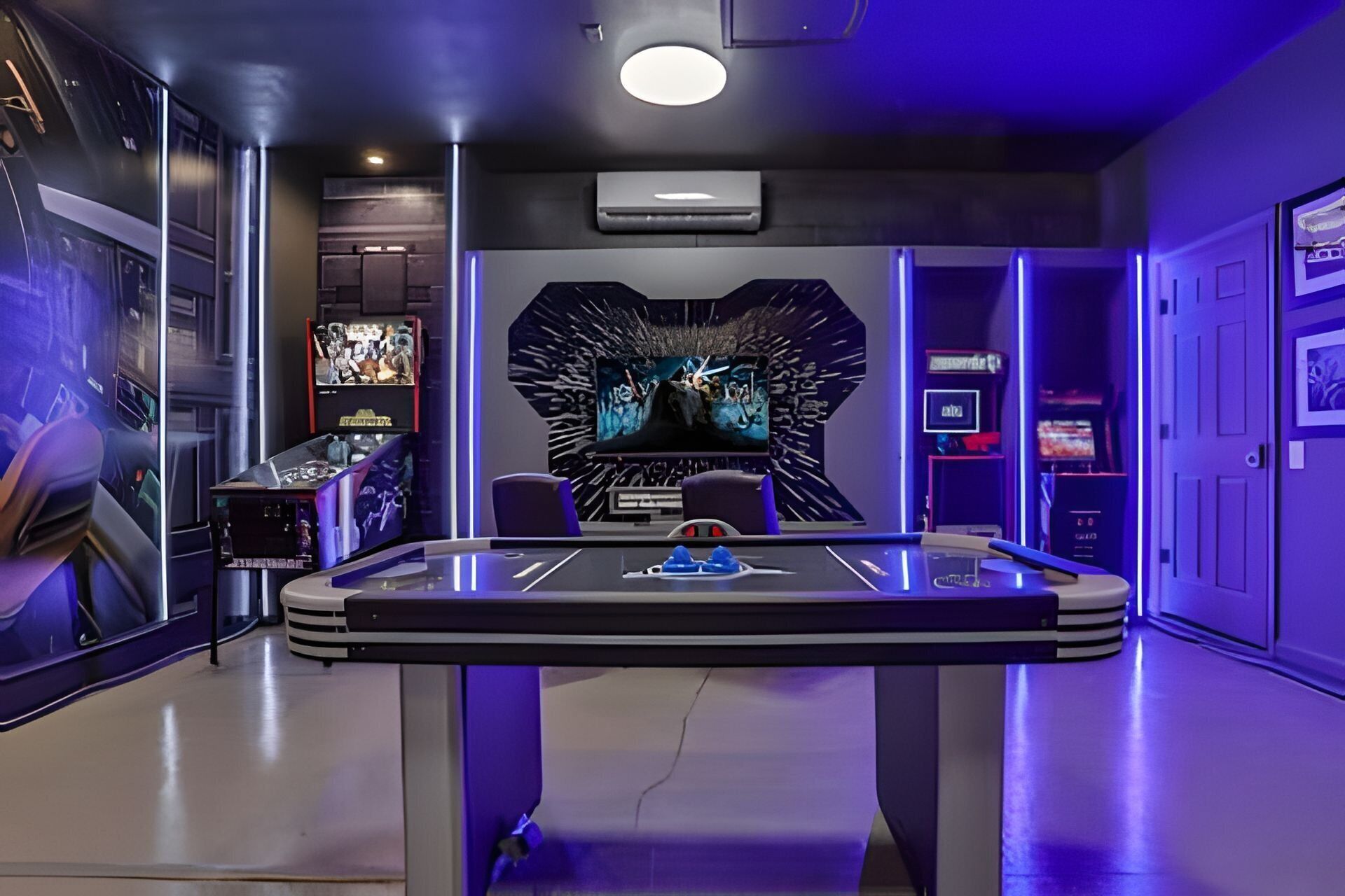 Una habitación con mesa de billar, juegos de arcade y una pantalla grande mostrando una película.