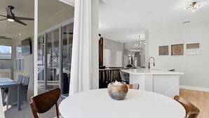 A modern kitchen with a central island, a dining area with a round table, and a view of the city through large windows.