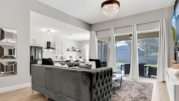 A modern living room with a grey sofa, a chandelier, and a view of the outdoors.
