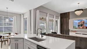 A modern kitchen with a large island, white cabinetry, and a built-in oven.