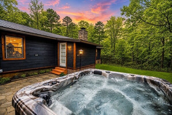 A wooden cabin with a hot tub, a chimney, and a porch.