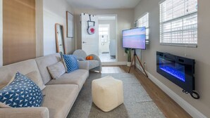 A living room with a sofa, ottoman, and a flat-screen TV mounted on the wall. - Comfort & Style Modern | 2BR In West Palm Beach (West Palm Beach)