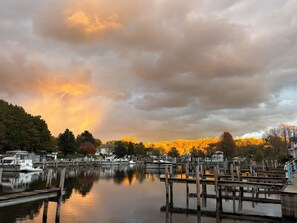Ein Yachthafen mit vertäuten Booten, hölzernen Stegen und im Hintergrund herbstlich gef ärbten Bäumen unter einem bewölkten Himmel.