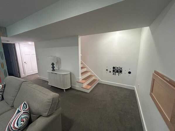 A living room with a gray sofa, a small white side table, a lamp, and a staircase leading to another level.