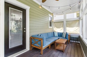 A covered porch with a blue sofa, wooden coffee table, and string lights.