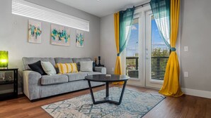 A modern living room with a grey sofa, a round black coffee table, and a patterned rug. - Cozy Luxury 1bd | Pool+Gym+Stockyards+Free Parking (Fort Worth)