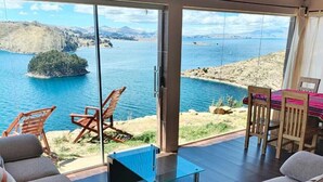 Un salon moderne avec une table en verre, des canapés et une vue sur un lac et des montagnes.