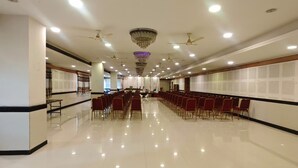A spacious hall with rows of red chairs, ceiling fans, and chandeliers.