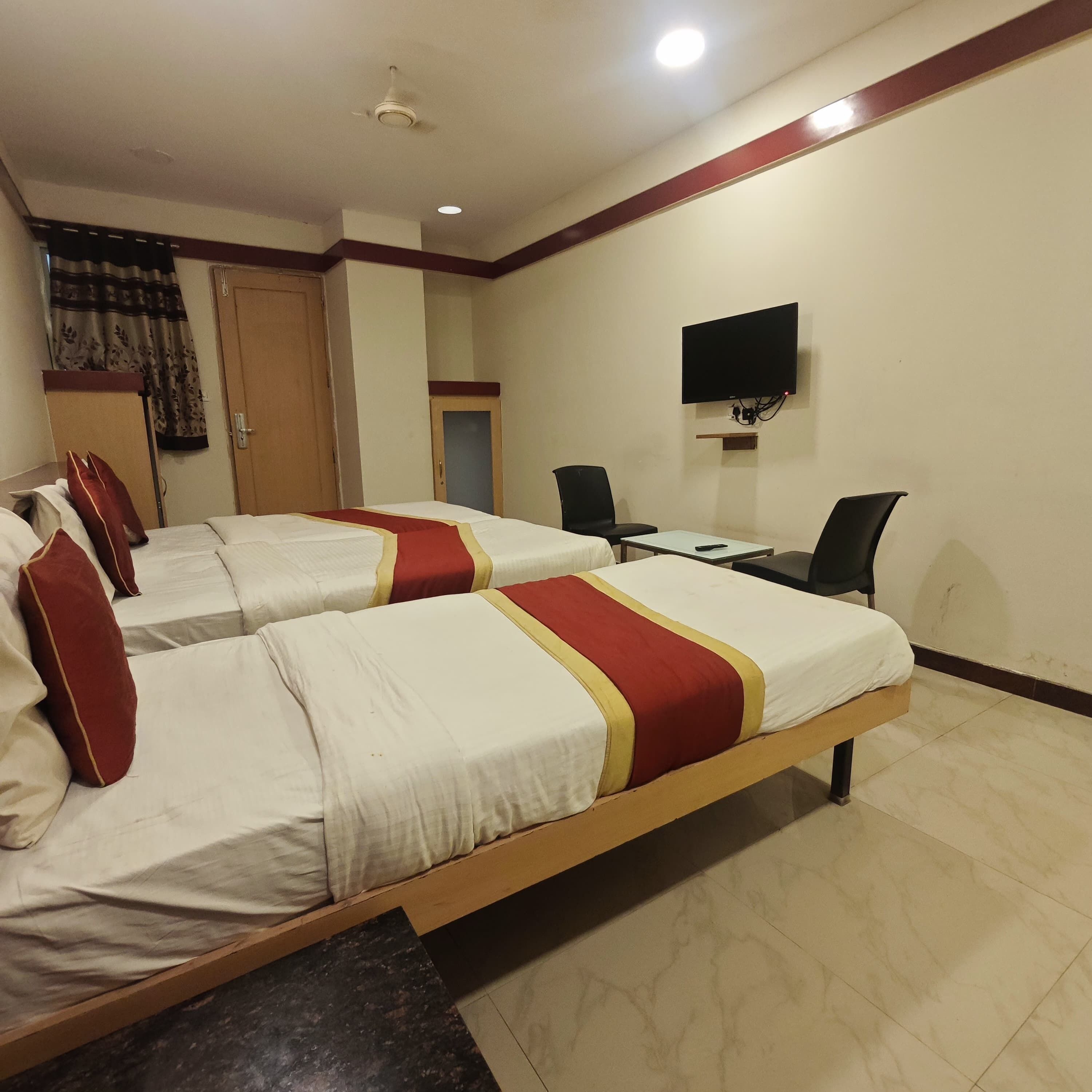 A hotel room with two beds, a desk, a chair, a TV, and a door.