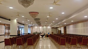A large hall with rows of red chairs, a stage with a podium, and ceiling fans.