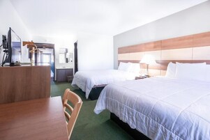 A hotel room with two beds, a desk with a chair, and a television.