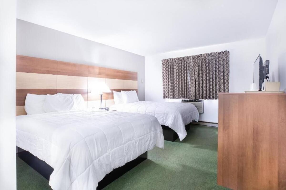 Habitación de hotel con dos camas, un escritorio, una lámpara y cortina estampada.