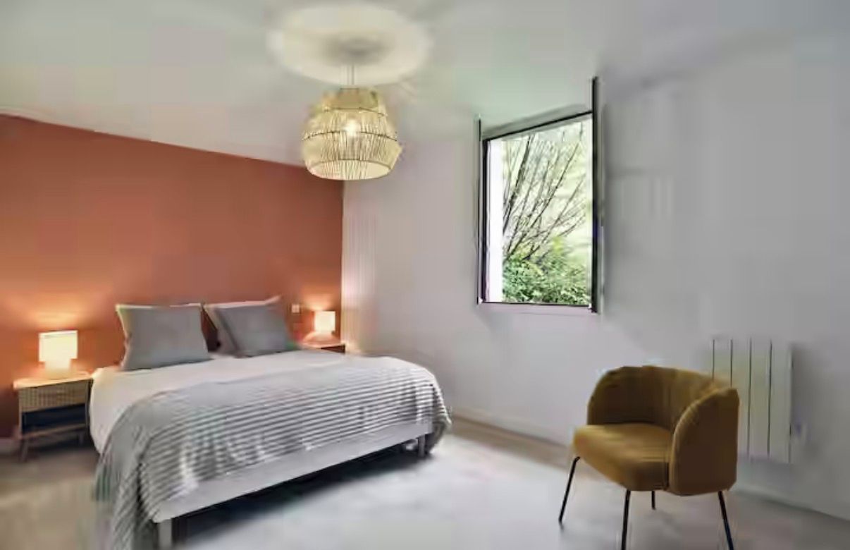Une chambre à coucher moderne avec un lit, des lampes de chevet, une chaise et une grande fenêtre.
