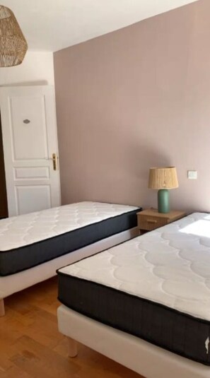 Une chambre avec deux lits simples, une table de chevet en bois avec une lampe et une porte.