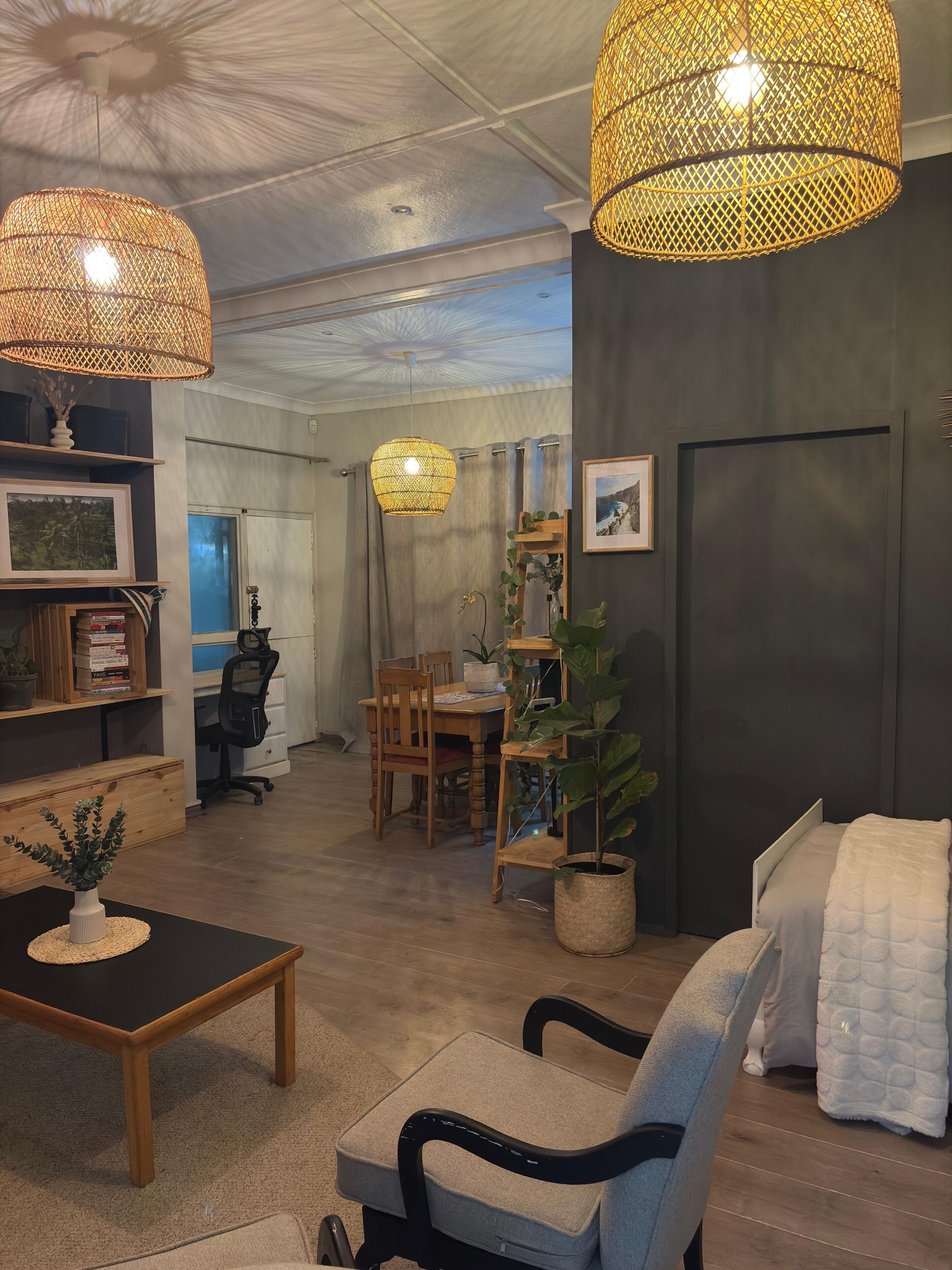 Ett modernt vardagsrum med en soffa, en fåtölj och ett matbord. Det finns två lampor av rotting, en krukväxt och en inramad tavla på väggen.