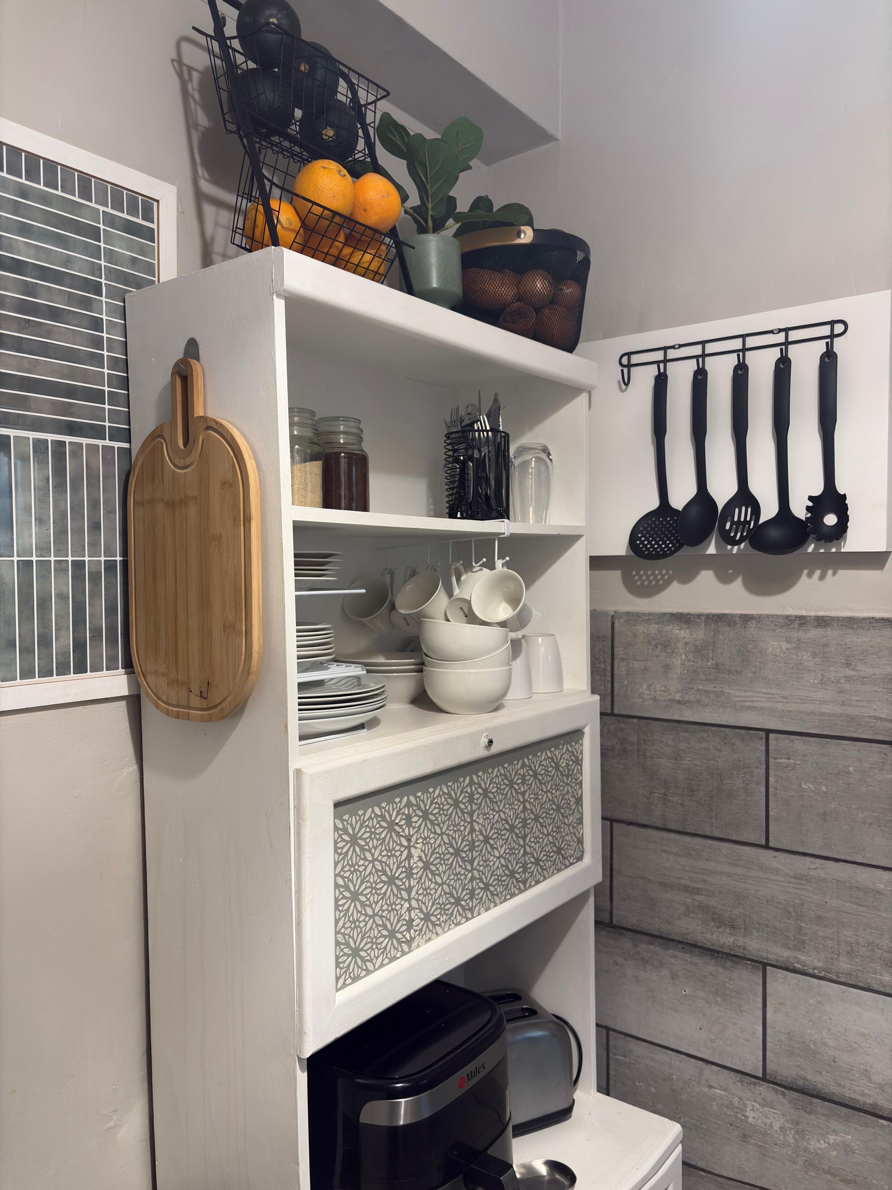 A kitchen with a wooden cutting board, a shelf with kitchen utensils, and a hanging rack with pots and pans.