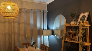 Un coin repas avec une table et des chaises en bois, un luminaire suspendu, un miroir et une étagère en bois ornée d’objets décoratifs.