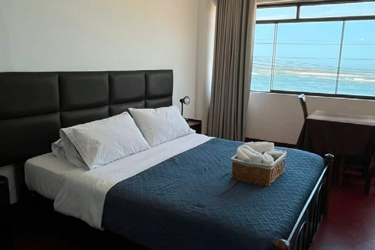 A hotel room with a bed, a desk, and a view of the ocean.