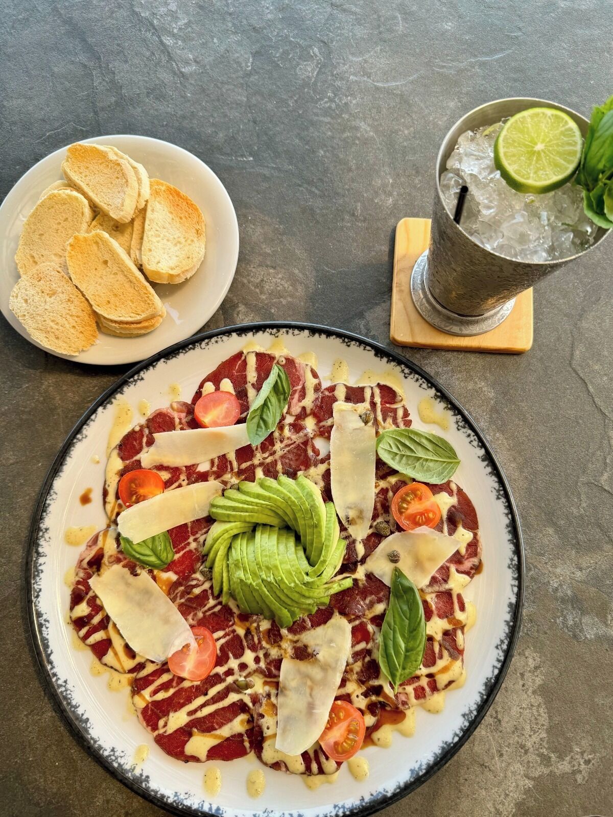 A plate of bruschetta with tomatoes, basil, and cheese, accompanied by a drink with a lime slice and mint leaves.