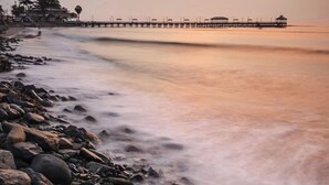 A rocky beach with a pier extending into calm waters. - Los Esteros (Huanchaco)
