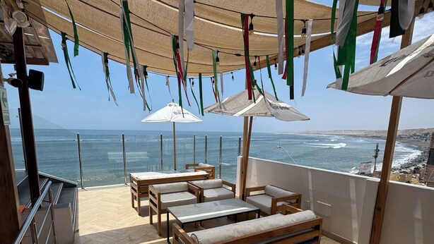 A sunlit outdoor seating area with wooden furniture and umbrellas, overlooking the sea. - Los Esteros (Huanchaco)