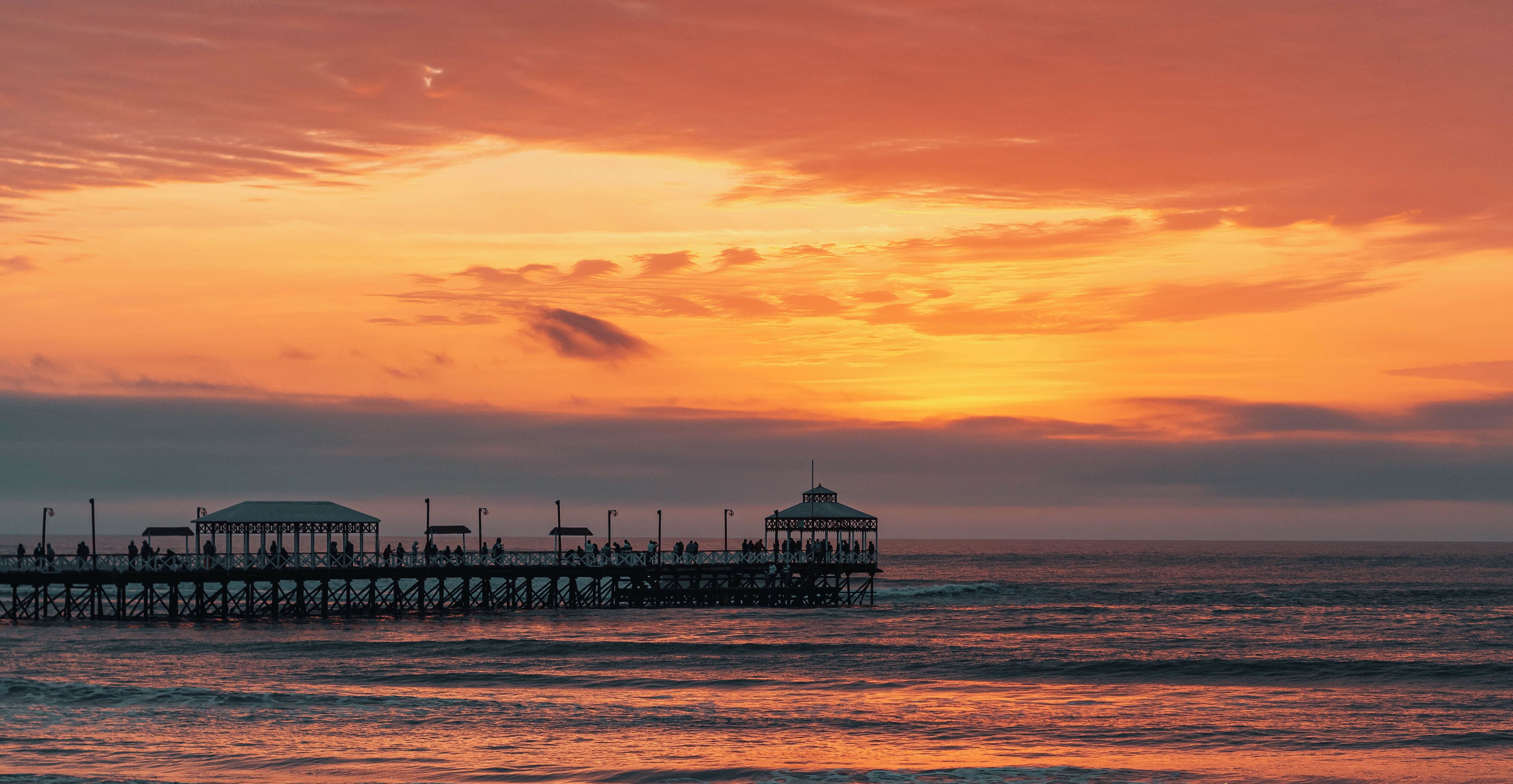 A pier extending into the sea with a sunset in the background.