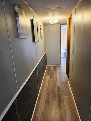 A narrow hallway with wooden flooring, a radiator, and a door leading to another room.