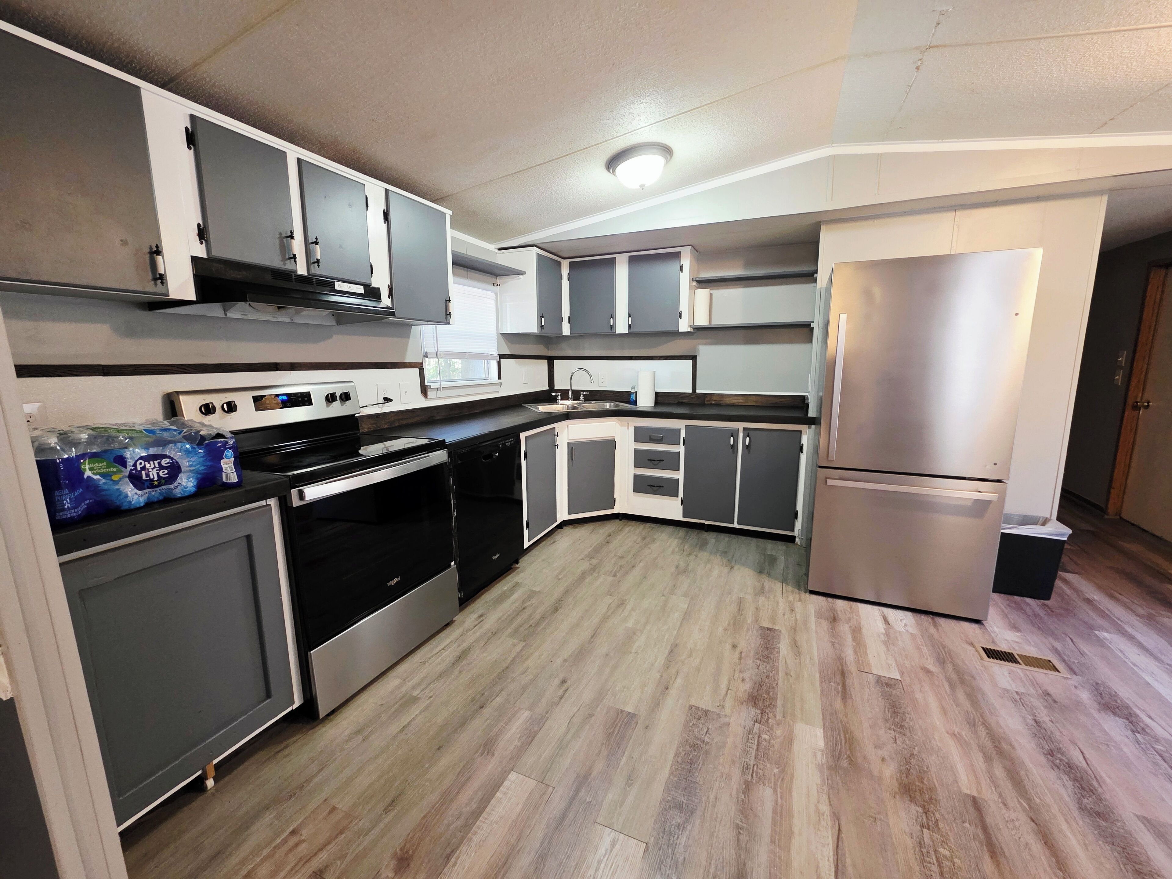A modern kitchen with stainless steel appliances, grey cabinets, and a wooden floor.