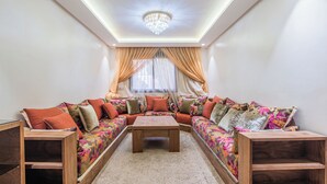 A modern living room with a sectional sofa, a wooden coffee table, and a chandelier. - Apartment with WiFi, Air conditioning, Parking, near Marina, Stadium and Souk (Agadir)