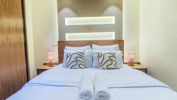 A neatly made bed with white linens, a wooden headboard, and two bedside lamps. - Apartment with WiFi, Air conditioning, Parking, near Marina, Stadium and Souk (Agadir)