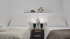 A bedroom with two beds, a nightstand with a lamp, and a shelf with decorative items. - Soul of Sal | 2-Bedroom, 2-Bathroom Central Apartment with Wi-Fi and A/C (Santa Maria)