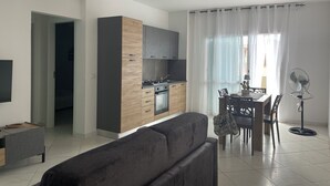 A modern kitchen with dark cabinets and a wooden countertop, a dining area with a table and chairs, and a grey sofa in the living area. - Soul of Sal | 2-Bedroom, 2-Bathroom Central Apartment with Wi-Fi and A/C (Santa Maria)
