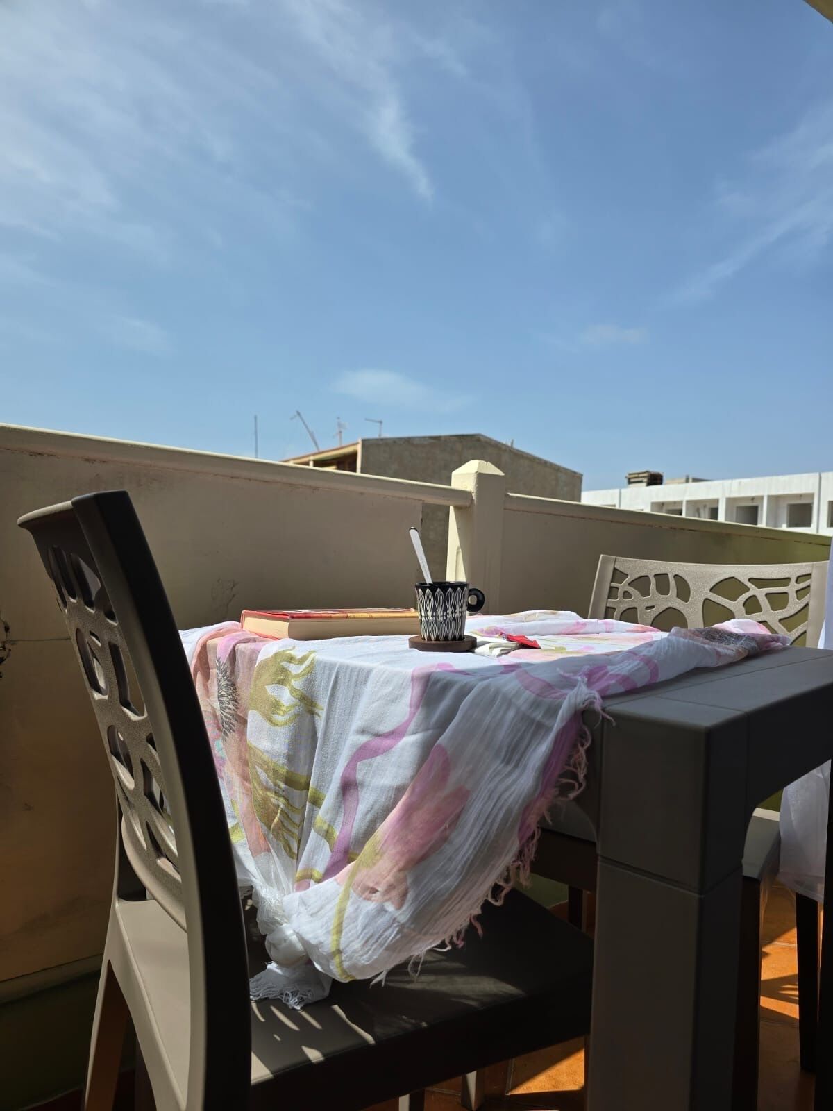 Een eethoek met een tafel, bedekt met een tafelkleed met bloemen, twee stoelen en een beker met rietje.