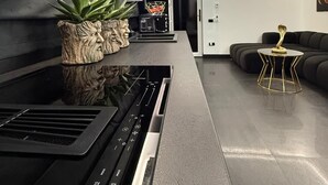 A modern kitchen with a built-in stove, a black countertop, and a seating area with a black sofa and a small round table. - Jas Pipera Studio &Private Pool (Voluntari)