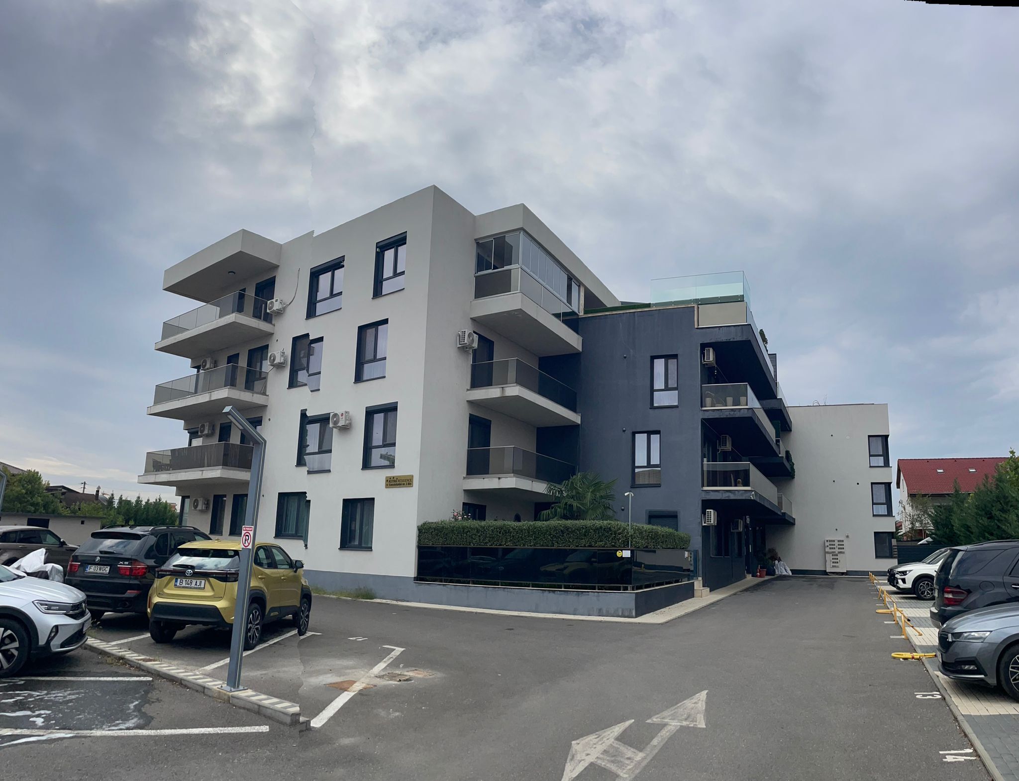 A multi-story residential building with balconies, a parking lot, and a clear sky.
