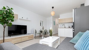 Un salon moderne comprenant un téléviseur à écran plat, un canapé, une table basse et un coin repas avec des chaises.