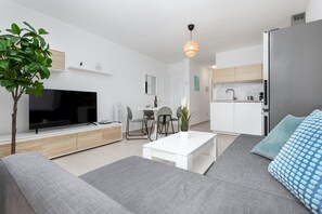 A modern living room with a flat-screen TV, a sofa, a coffee table, and a dining area with chairs. - Home2Book Sunny Terrace & Pool Costa Calma (Costa Calma)