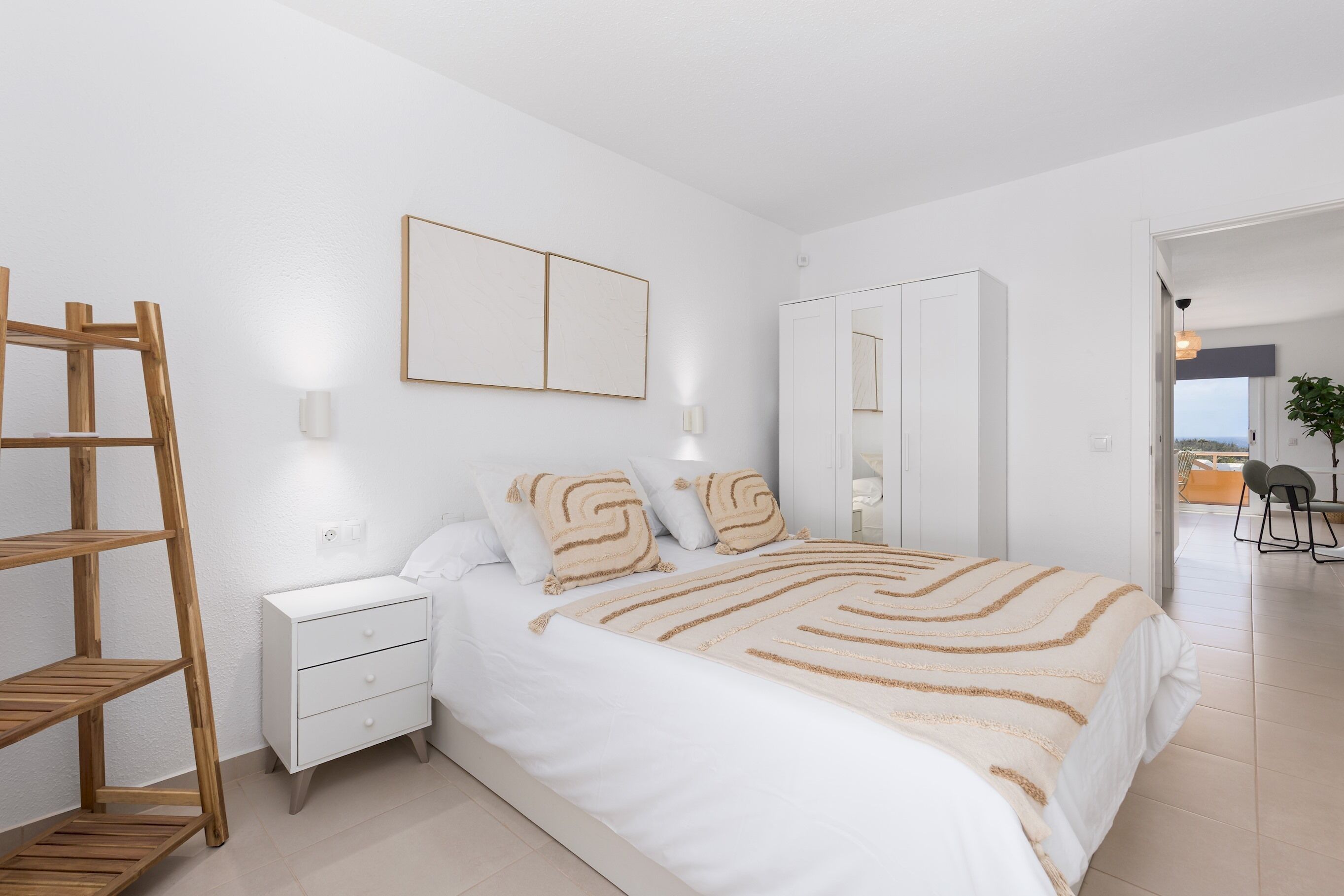 A bedroom with a bed, bedside tables, a wardrobe, a mirror, and a wooden ladder.