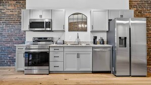Una cocina moderna con electrodomésticos de acero inoxidable, armarios blancos y una pared de ladrillo.