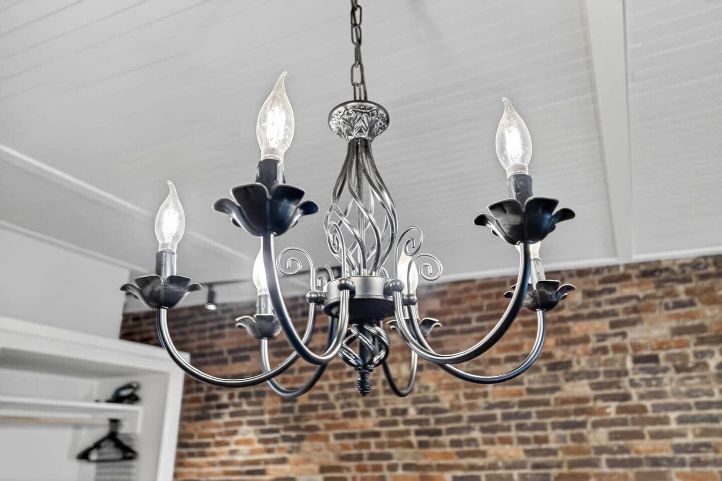 Un candelabro con una ornamentada estructura metálica central y cuatro brazos, cada uno con una bombilla al final.