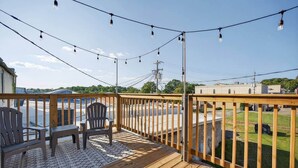 A wooden deck with two Adirondack chairs, a string of lights, and a view of a parking lot and buildings in the background. - Sleeps 6. Two Downtown Lofts Combined. (Fayetteville)