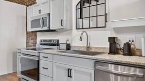 A modern kitchen with white cabinetry, a stainless steel dishwasher, a built-in oven, a microwave, a toaster, and a coffee maker. - Sleeps 6. Two Downtown Lofts Combined. (Fayetteville)