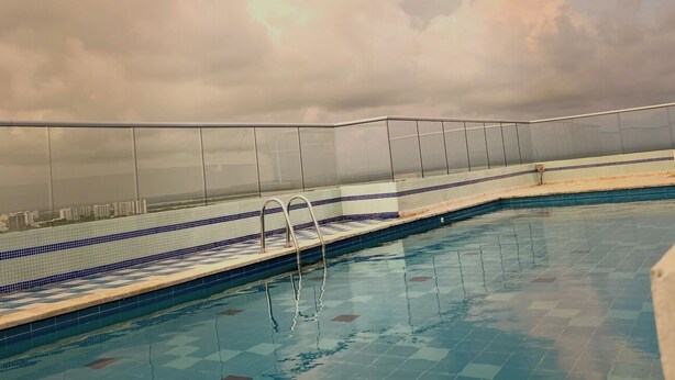 An indoor swimming pool with clear blue water, a tiled deck, and a cloudy sky in the background. - Apartment 5 minutes from the Sea and Downtown Airport (Cartagena de Indias)