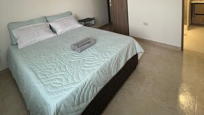 A modern bedroom with a large bed, a nightstand, a wooden wardrobe, and an air conditioning unit on the wall. - Apartment 5 minutes from the Sea and Downtown Airport (Cartagena de Indias)