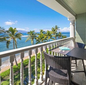 A balcony with a view of the ocean, palm trees, and a table with chairs. - Stunning Views from 5th-Floor Oceanfront Retreat (Lahaina)