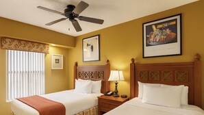 Une chambre d’hôtel avec deux lits, un ventilateur de plafond, une fenêtre avec des stores et des œuvres d’art accrochées aux murs.