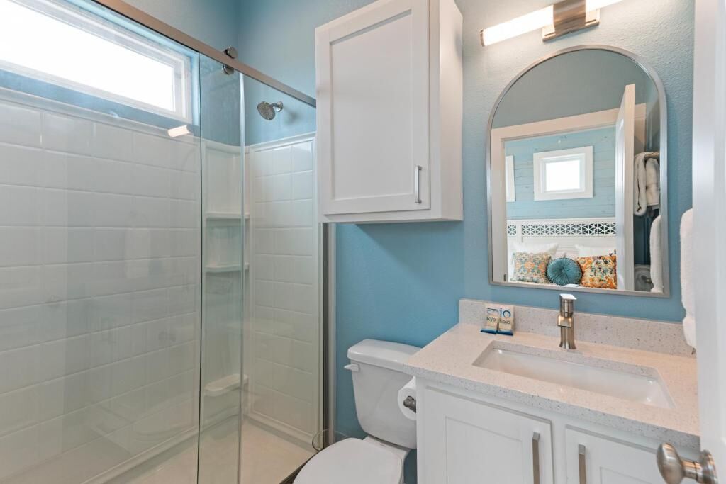 Une salle de bain avec une douche à parois de verre, des toilettes blanches, un lavabo avec un miroir au-dessus et un porte-serviettes.