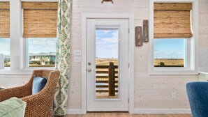 Ein Zimmer mit einem Korbstuhl, einer Holztür und zwei Fenster mit Jalousien.